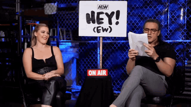 a man and a woman are sitting in front of a sign that says hey ew