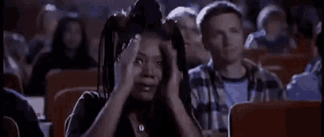a woman is screaming in a movie theater while sitting in a crowd of people .
