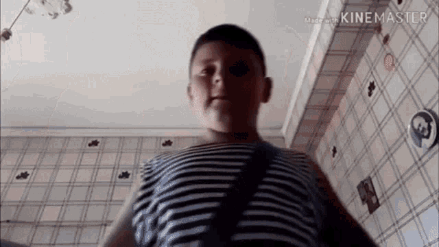 a young boy in a striped shirt is standing in front of a checkered wall and looking at the camera .