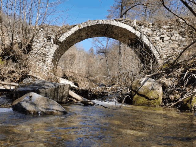 a stone bridge over a river with a blue sky in the background