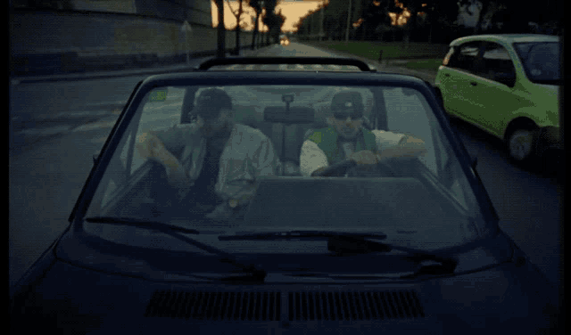 two men are sitting in a car and one is wearing a green shirt