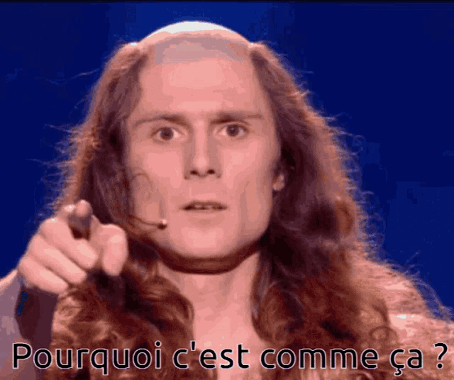 a man with long hair is pointing at the camera with the words pourquoi c'est comme ca