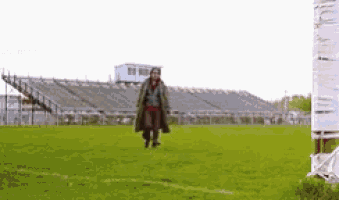 a man in a trench coat is walking on a football field