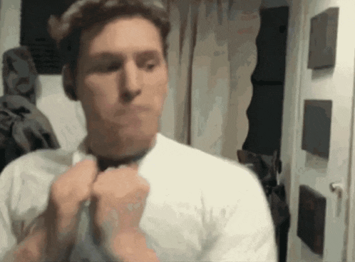 a man in a white shirt adjusts his tie in front of a mirror