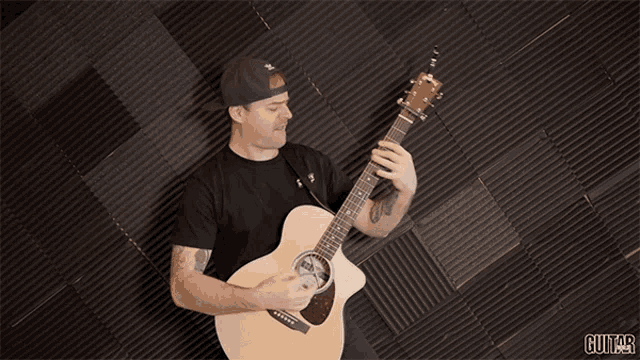 a man is playing an acoustic guitar in front of a black wall with the word guitar on it