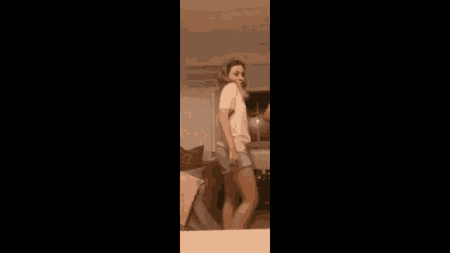 a woman is dancing in a living room while wearing shorts and a white shirt .