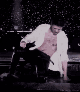 a man in a white shirt and black pants is kneeling down on a stage with blondejongin written below him