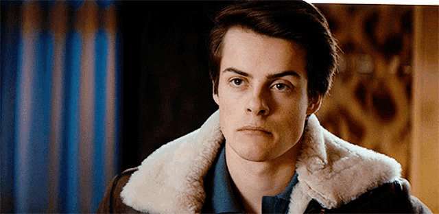 a man wearing a fur collared jacket looks at the camera
