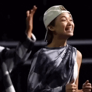 a woman wearing a baseball cap and a gray shirt is laughing and raising her hand in the air .