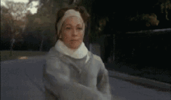 a woman wearing a headband and a gray jacket is running down a street .