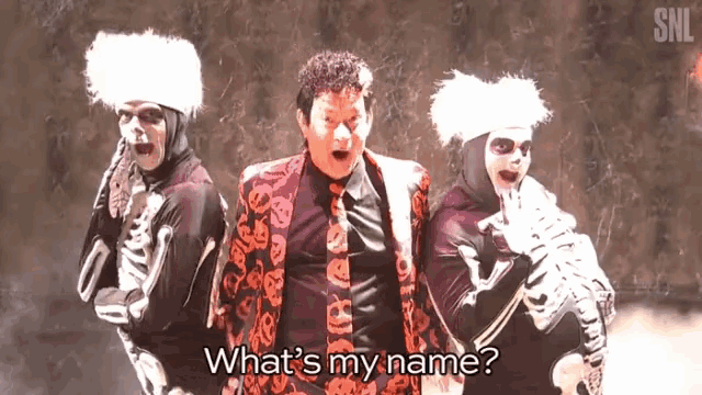 a man in a suit and tie is standing next to two skeletons and asking what 's my name