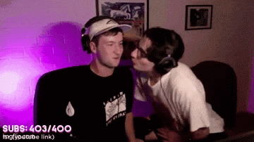 a man is kissing another man on the cheek while wearing headphones and a hat .