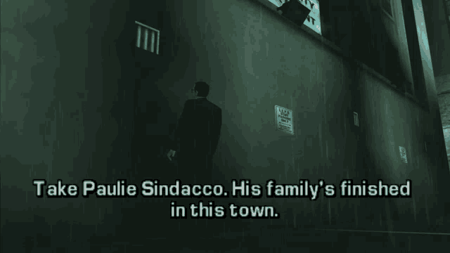 a man in a suit stands in front of a wall that says take paulie sindacco