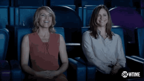 two women sit in a theater with showtime written on the bottom right