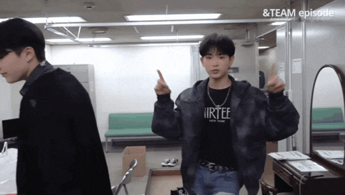a man wearing a black shirt that says " irtee " stands in a room