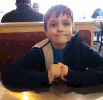 a young boy is sitting at a table in a diner making a funny face