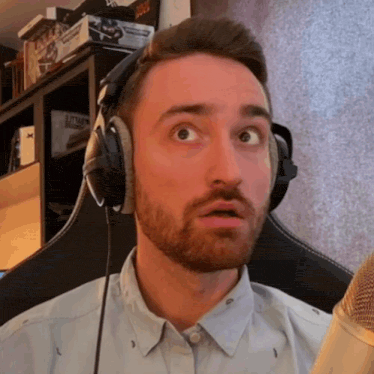 a man with a beard wearing headphones and a microphone making a surprised face