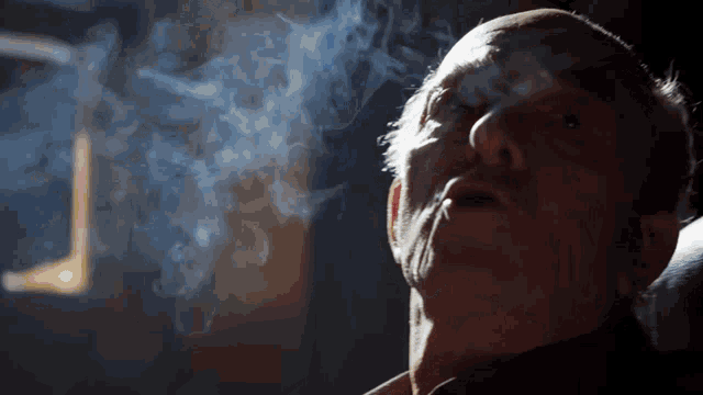 a man is smoking a cigarette in a dark room with smoke coming out of his mouth