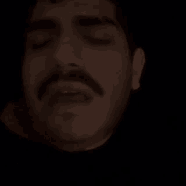 a close up of a man 's face with his eyes closed and a mustache in the dark .