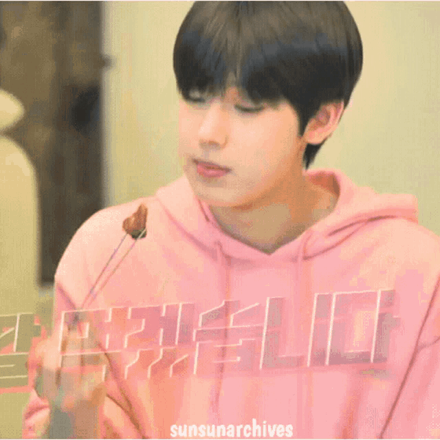 a boy wearing a pink hoodie is eating a piece of chocolate