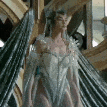 a woman in a white dress with wings and a crown is standing in front of a mirror .