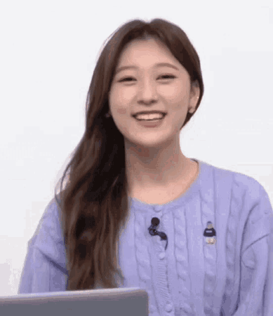 a woman in a purple sweater is smiling and sitting in front of a laptop .