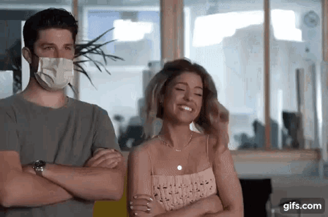 a man wearing a face mask is standing next to a woman .