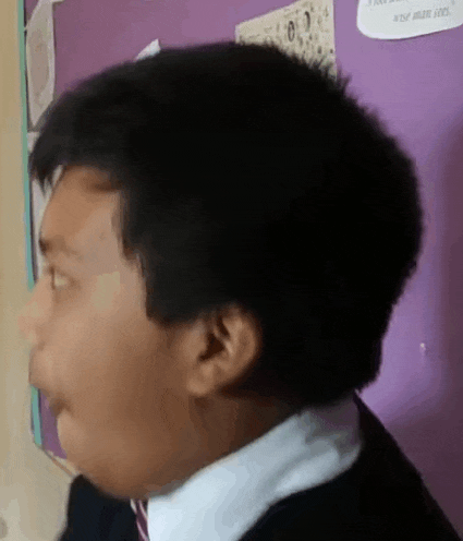 a young boy in a suit and tie is making a funny face in front of a purple wall .