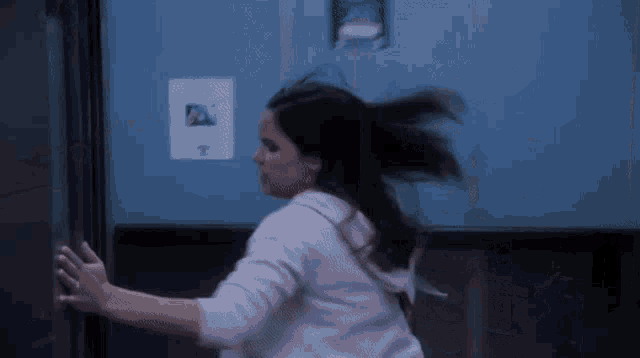 a woman in a white sweatshirt is running in front of a blue wall with a picture on it that says t.