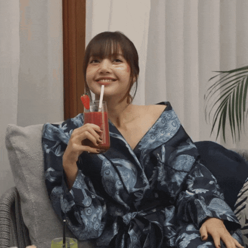 a woman in a blue robe is holding a glass of red liquid