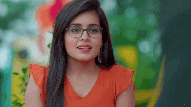 a woman wearing glasses and an orange shirt is smiling for the camera