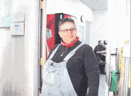 a woman wearing overalls and a bandana stands in front of a vending machine