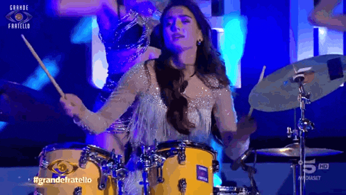 a woman is playing drums on a stage with the words grande fratello on the bottom right
