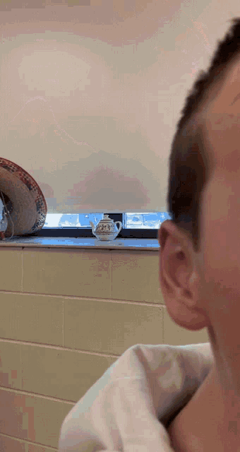 a man looks out a window at a teapot on a window sill