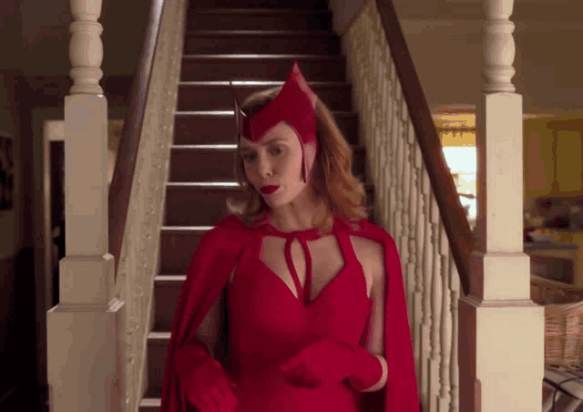 a woman in a red cape and gloves stands in front of stairs