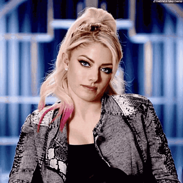a woman with blonde hair and blue eyes is wearing a grey jacket with a snake print