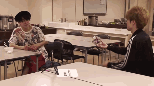 two young men are sitting at a table and one of them is holding something in his hand that says ' a ' on it
