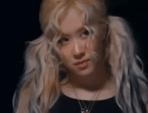 a woman with blonde hair and pigtails is wearing a black top and necklace .