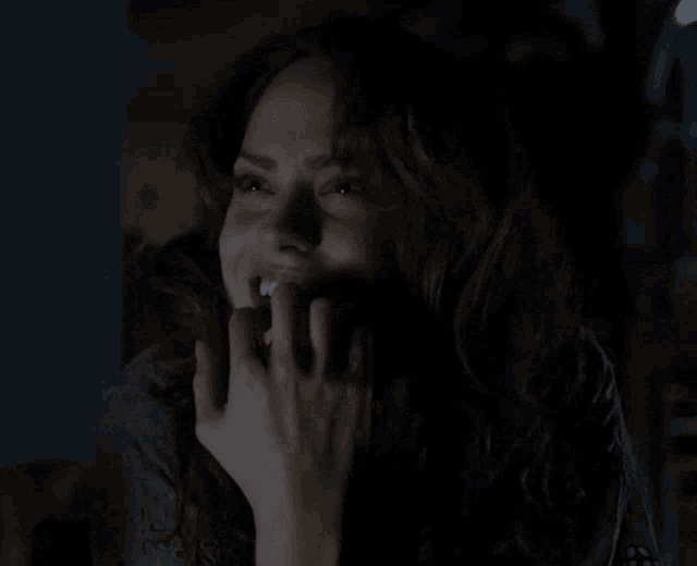 a woman is smiling in the dark with her hand on her face