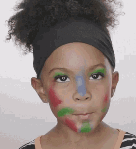 a little girl with her face painted in different colors is wearing a headband .