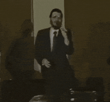 a man in a suit and tie is singing into a microphone while standing in a dark room .