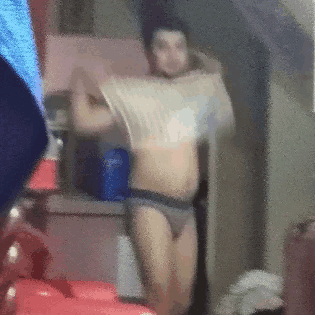 a man in underwear is standing in a room holding a shirt over his head .