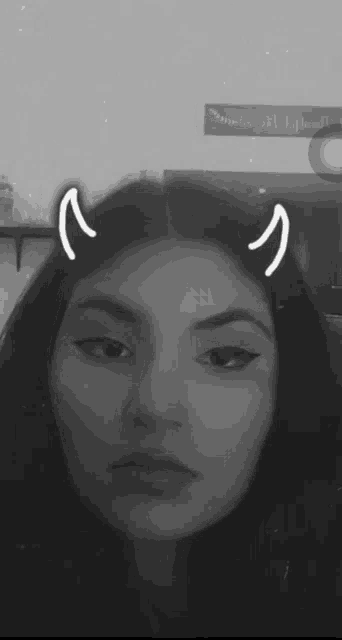 a woman with devil horns in her hair is taking a selfie in a black and white photo .