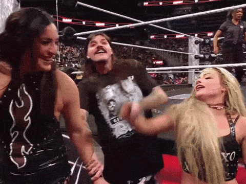 a man wearing a shirt that says ' g ' on it is laughing with two women in a wrestling ring