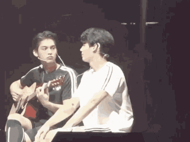 a man is playing a guitar and another man is sitting next to him .