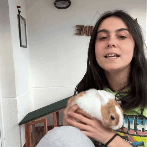 a woman holding a small rabbit in front of a sign that says eme