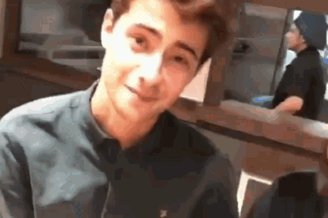 a young man in a black shirt is smiling and looking at the camera while a man in a black hat is behind him .