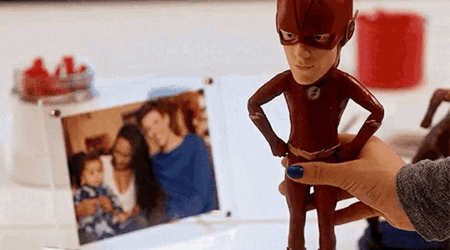 a person is holding a flash figure in front of a picture of a family .