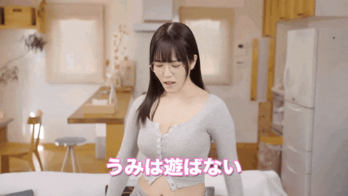 a woman in a grey sweater is sitting on a bed in a room with chinese writing on the bottom