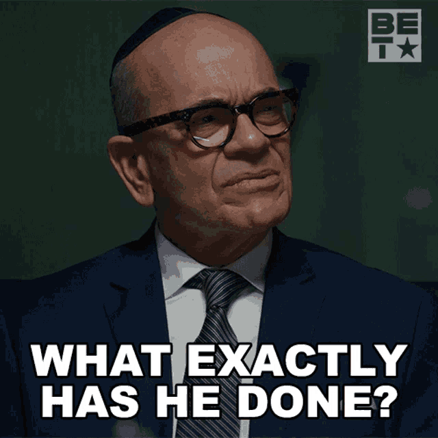 a man wearing glasses and a suit says what exactly has he done